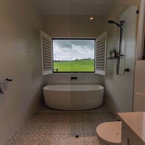 Une salle de bain avec une grande baignoire, des toilettes et une fenêtre donnant sur un champ verdoyant.