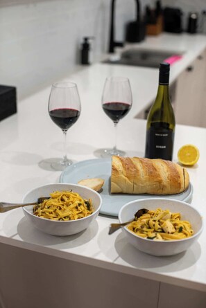 A dining table with two glasses of red wine, a bottle of wine, and two bowls of pasta. - The Old Farm Cottage, Mount Torrens (Mount Torrens)