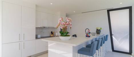 A modern kitchen with white cabinets, a central island with bar stools, and a decorative orchid plant.