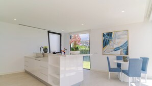 A modern kitchen with a central island, white cabinetry, and a dining area with blue chairs. - Luxury Diamond House (Funchal)