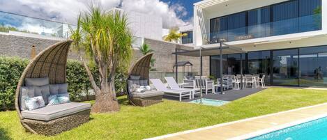 A modern outdoor pool area with a built-in seating area, a swimming pool, and a glass-enclosed building.