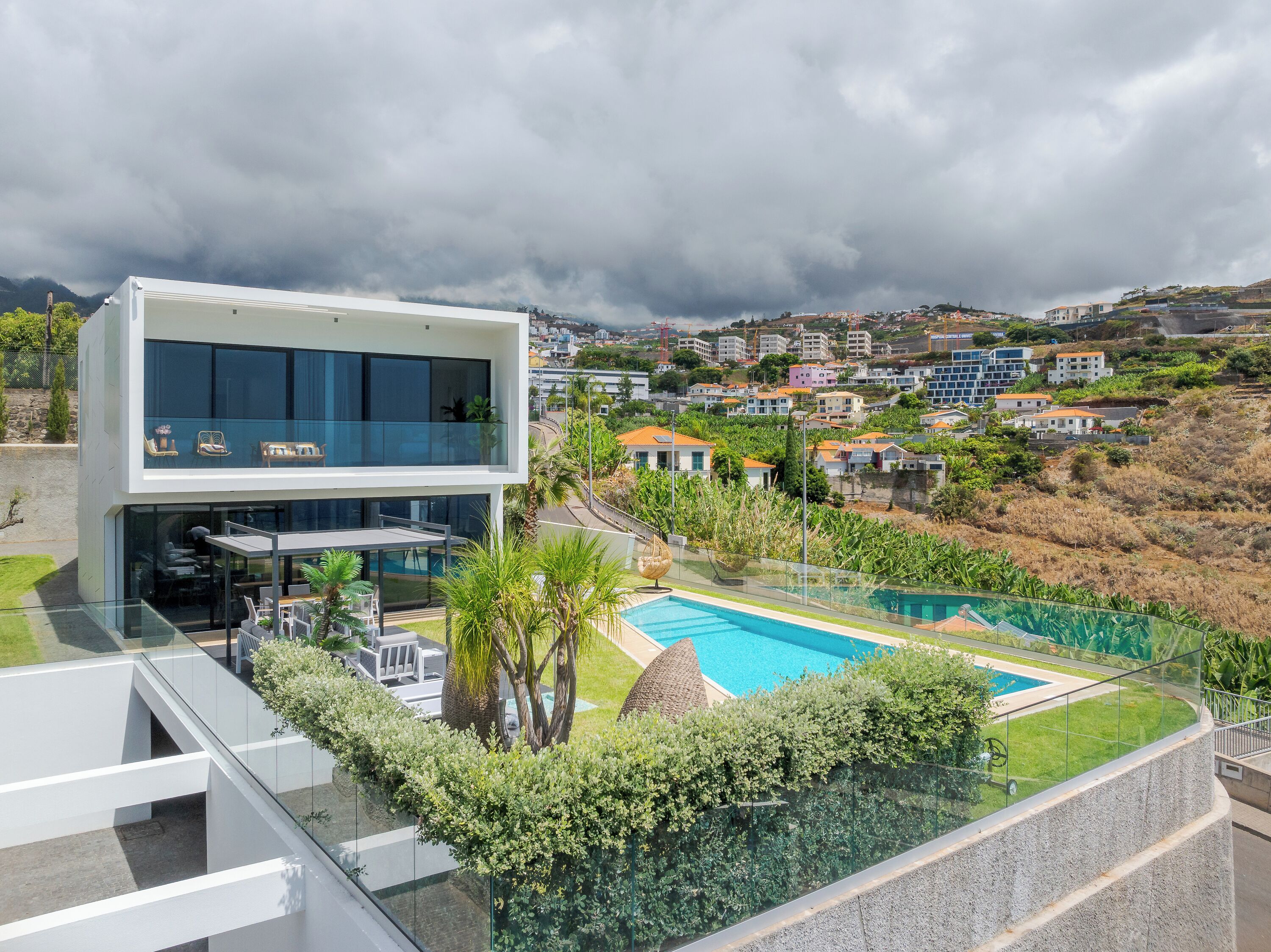 Ein modernes, zweistöckiges Gebäude mit einem Glasbalkon mit Blick auf einen Swimmingpool und üppiges Grün.