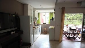 Cocina compacta con televisor, armarios y comedor con mesa y sillas.