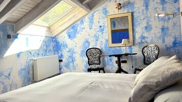 A room with a sloped ceiling, a skylight, a bed with white bedding, two zebra-patterned chairs, a small table, a wall-mounted mirror, and a radiator.