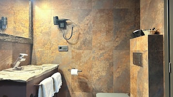 Un baño con pared de mármol, un lavamanos con toalla, ducha y cubo de basura.