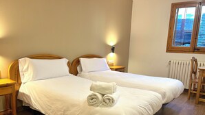 A double bed with white linens and two pillows, a wooden nightstand with a lamp, and a chair with a wooden frame. - La Posada d'Àneu by RdA Hotels (Esterri D'Aneu)