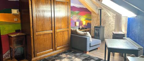 A cozy attic room with a wooden wardrobe, a sofa, a small table, and a colorful mural on the wall.