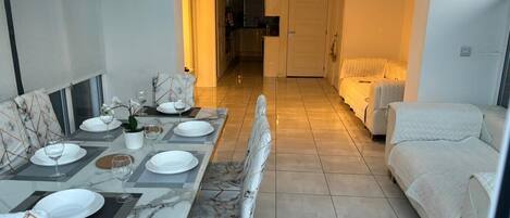 Un comedor con una mesa larga dispuesta para cuatro personas, un sofá y una cama al fondo.