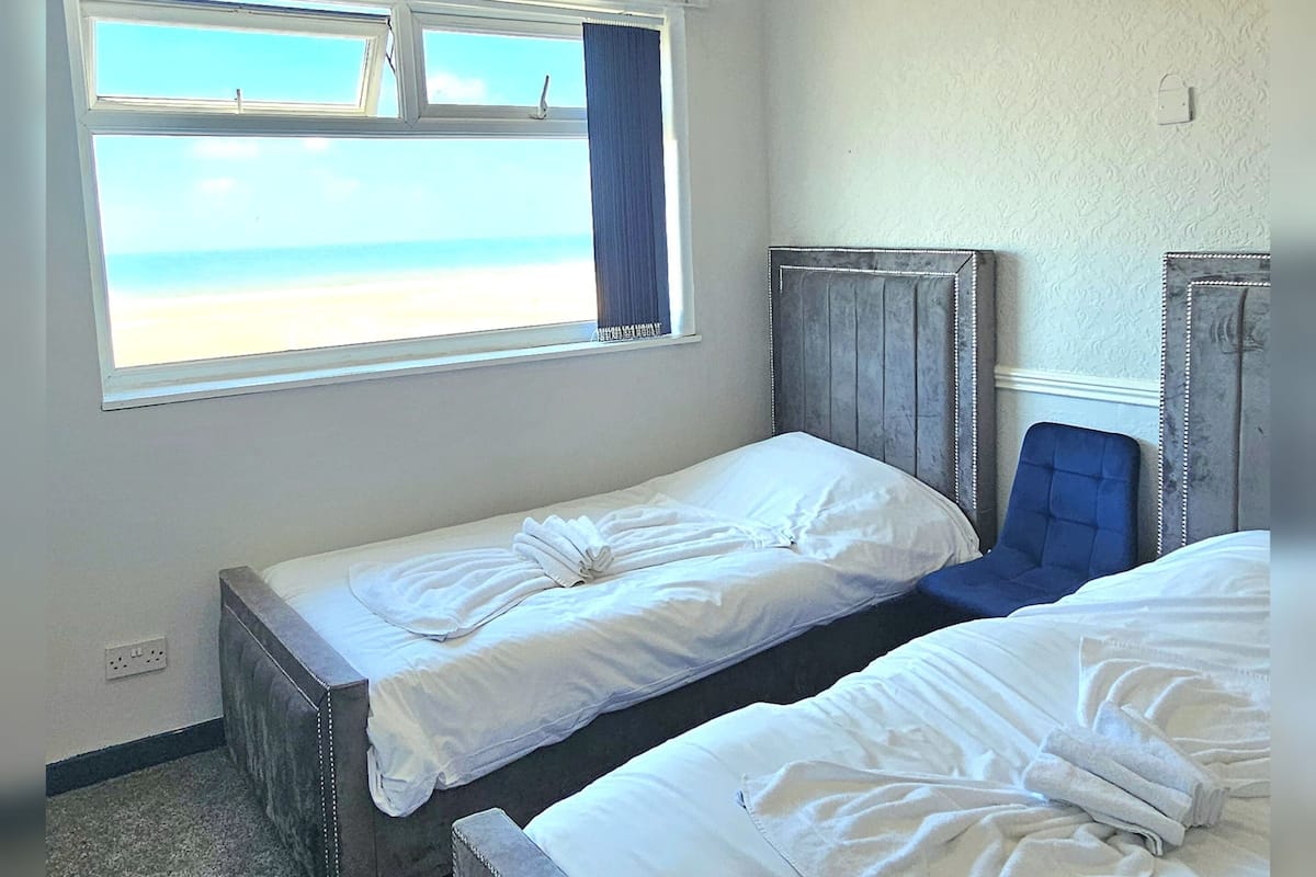 Una habitación con dos camas, un ventanal con vista a la playa y un cabecero con un panel decorativo.