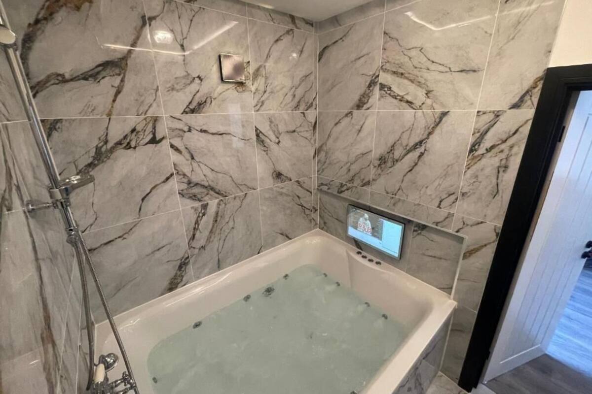 Un baño moderno con pared de mármol, una bañera y un panel de control digital.