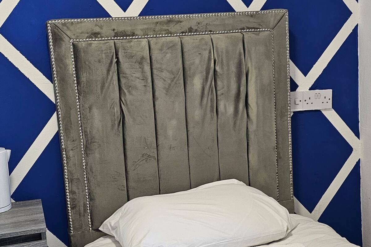 Una cama con cabecera gris tapizada frente a una pared azul con diseños geométricos blancos.