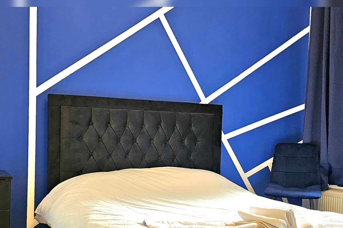 Una cama con cabecera capitonada, ropa de cama blanca y una toalla doblada sobre la cama.