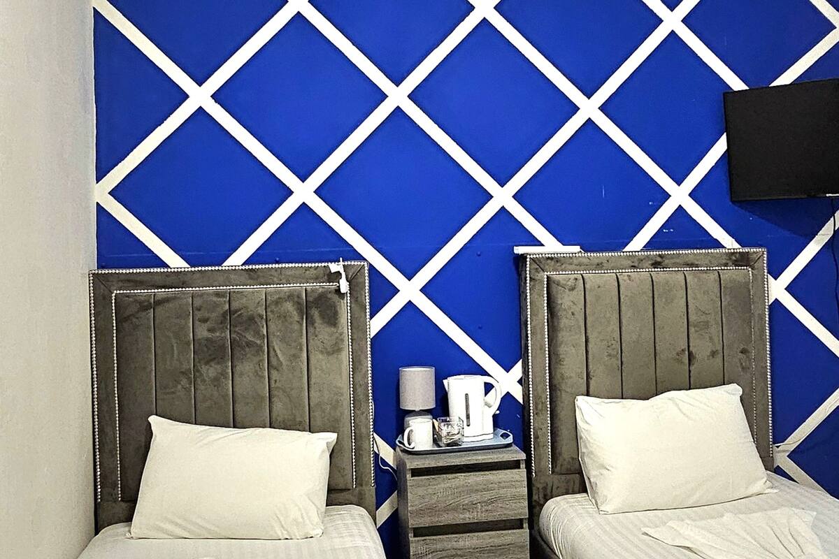 Una habitación con dos camas, una mesita de noche con lámpara y un televisor montado en la pared.