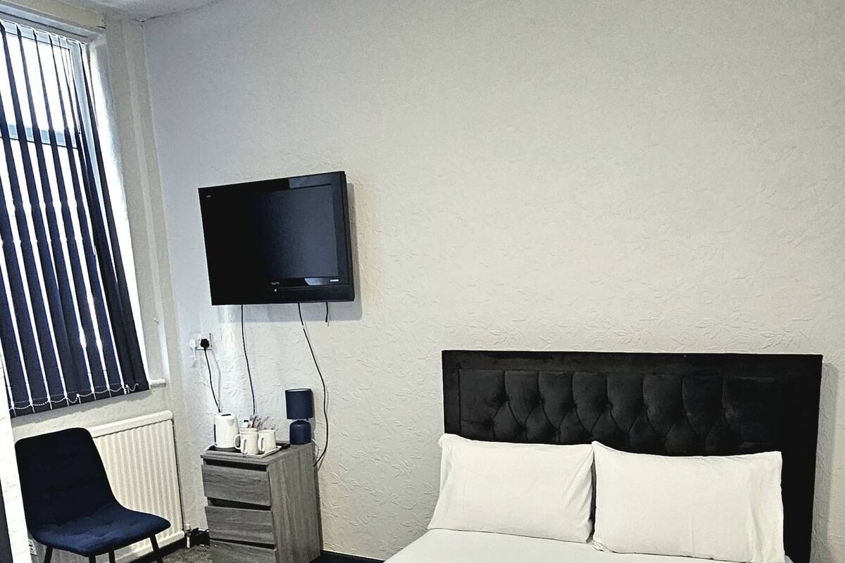 Una habitación de hotel con cama, una silla, tocador, televisor y ventana con persianas.