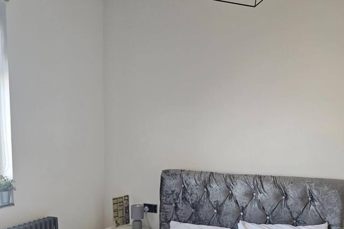 Un dormitorio con cama, mesita de noche, radiador y ventana.