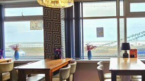 A dining area with a wooden table and chairs, a decorative column, and a view of the sea through large windows. - Sapphire Hotel Blackpool (Blackpool)