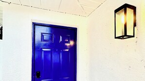 A blue door with a keyhole and a handle, a light fixture on the wall, and a ceiling with a grid pattern. - Modern Studio w/ Private Bath, Fast Wi-Fi, Laundry (Zephyrhills)