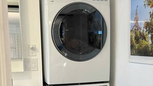 A stacked washer and dryer unit in a small laundry room with a sink and a framed picture on the wall. - Modern Studio w/ Private Bath, Fast Wi-Fi, Laundry (Zephyrhills)