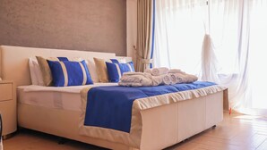 Ένα σύγχρονο δωμάτιο ξενοδοχείου με ένα μεγάλο κρεβάτι, λευκά κλινοσκεπάσματα και μπλε διακοσμητικά στοιχεία.