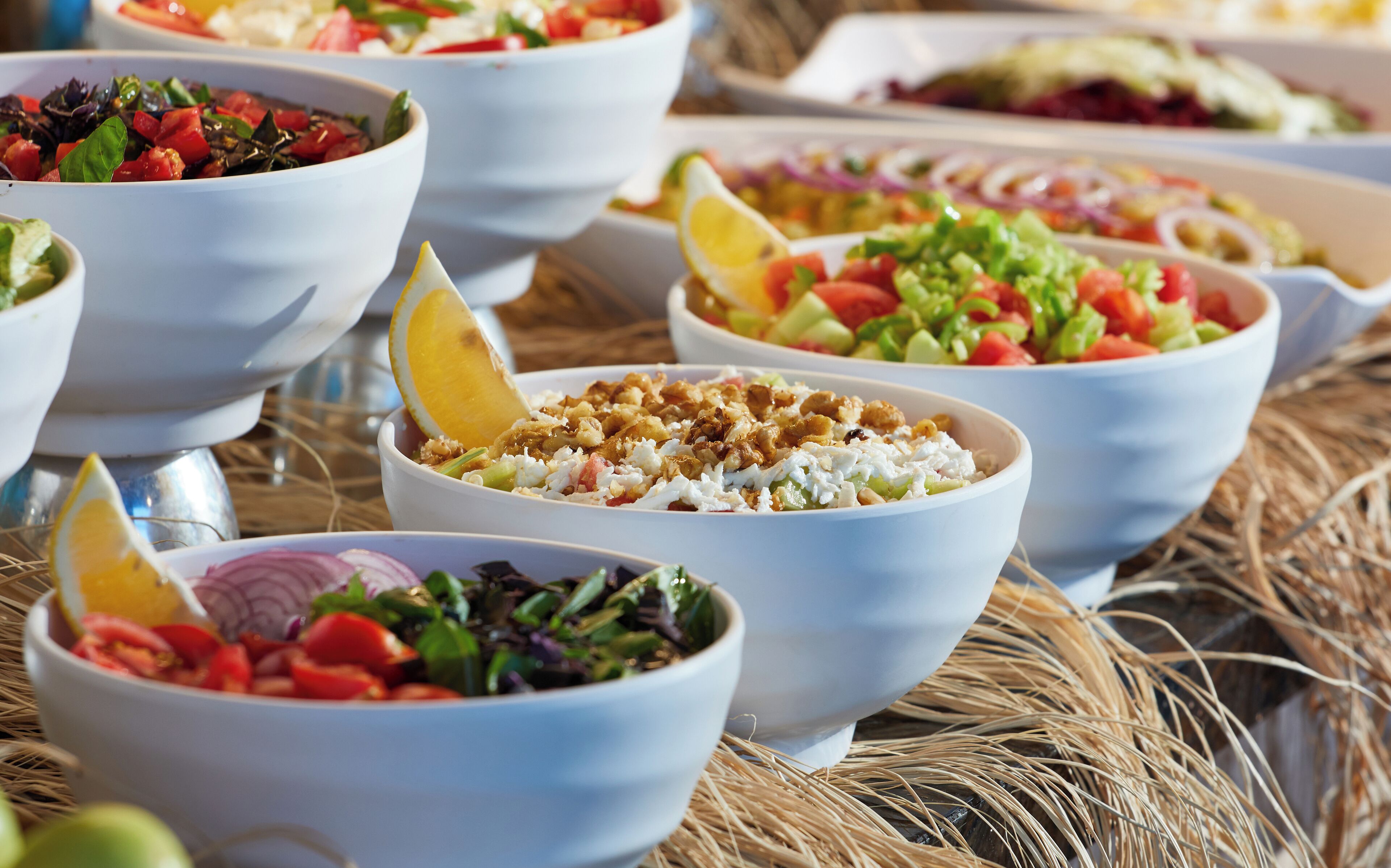 A variety of bowls containing different salads and fruits, arranged on a table with a rustic background.