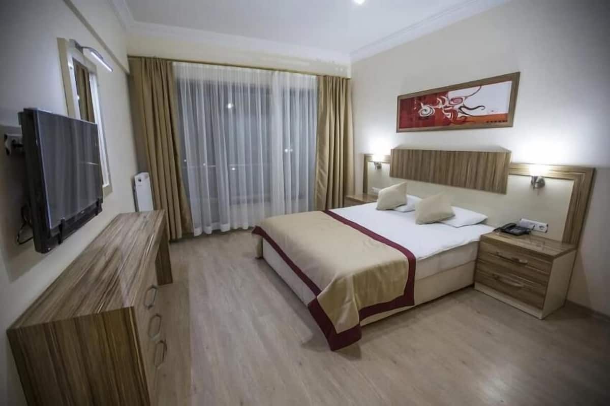 Ένα δωμάτιο ξενοδοχείου με ένα κρεβάτι, μια τηλεόραση, ένα γραφείο, ένα φωτιστικό και έναν πίνακα στον τοίχο.