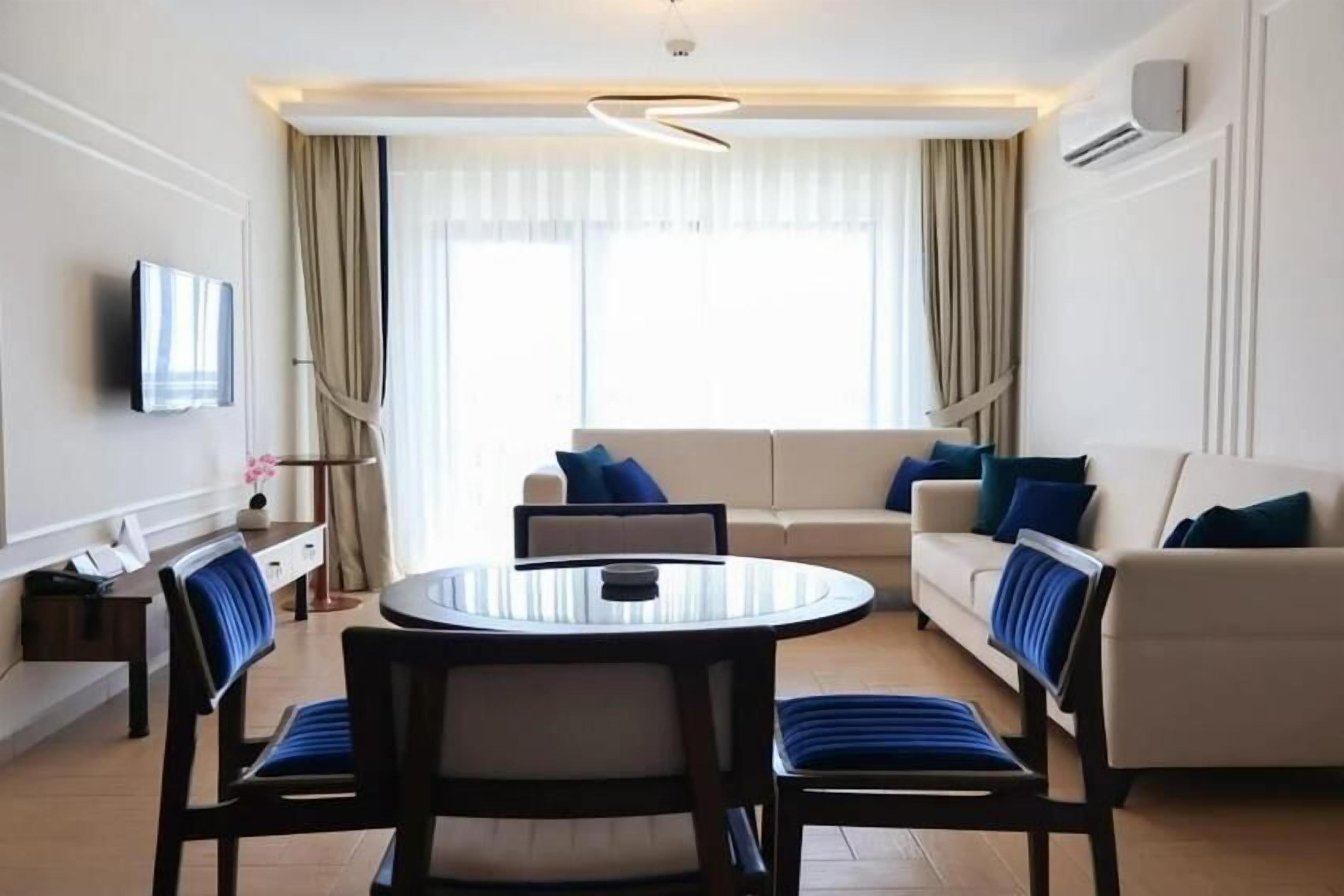 Una habitación de hotel moderna con una mesa redonda de comedor, dos sofás y un televisor montado en la pared.