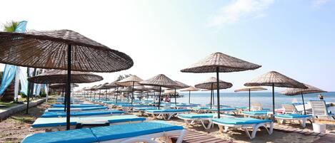 A beach with rows of sun loungers and thatched umbrellas.