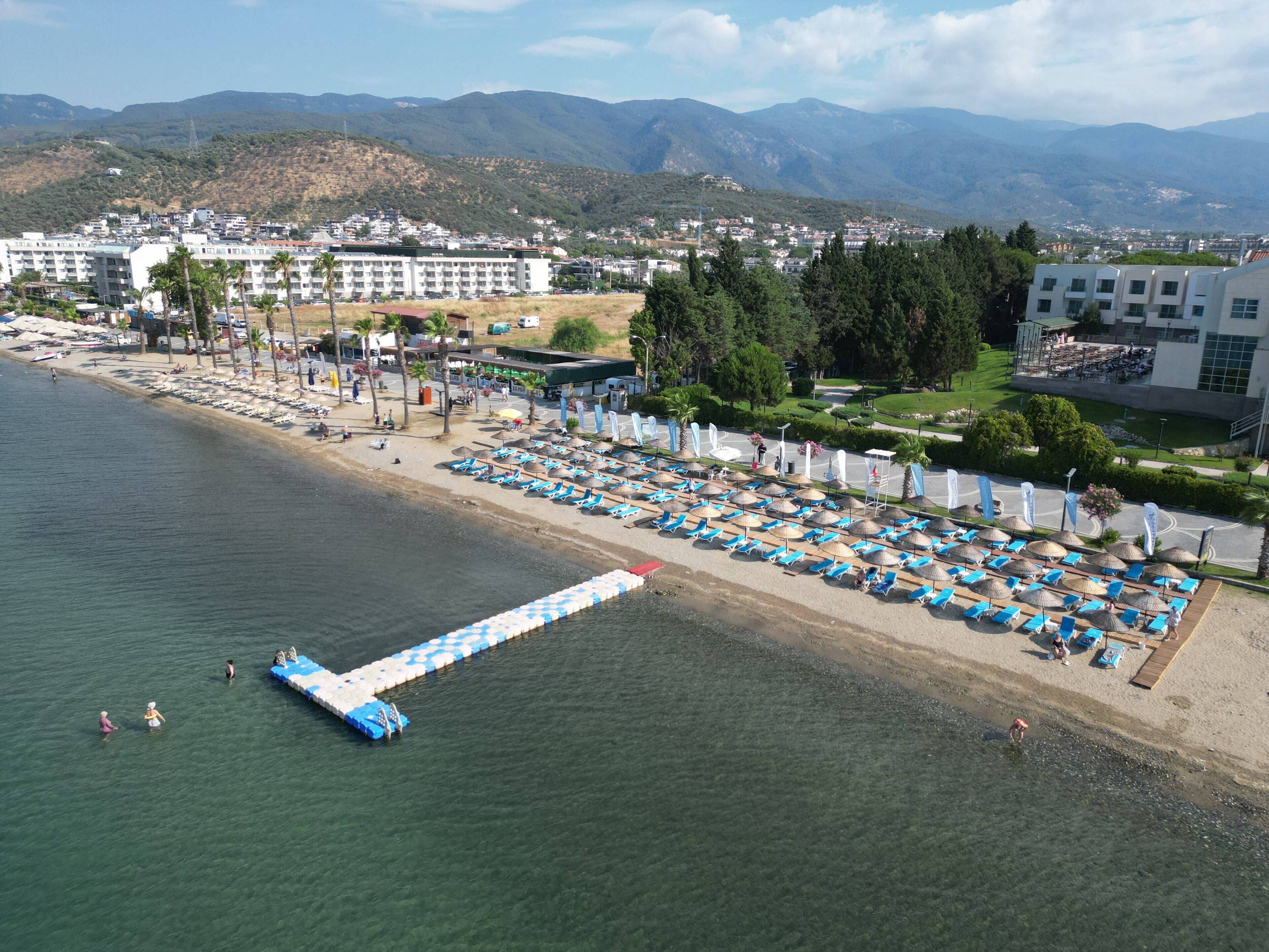 A coastal resort with a beach, lounge chairs, umbrellas, and a pier extending into the water.
