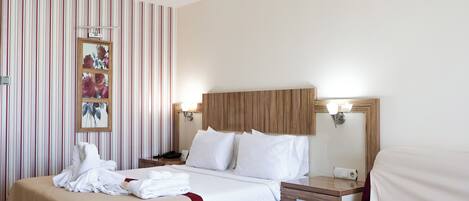 A hotel room with a large bed, a bedside table, a nightstand, a mirror, and a wall with striped wallpaper.
