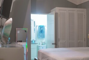 Quarto com cama, guarda-roupa e banheiro visível por uma porta aberta.