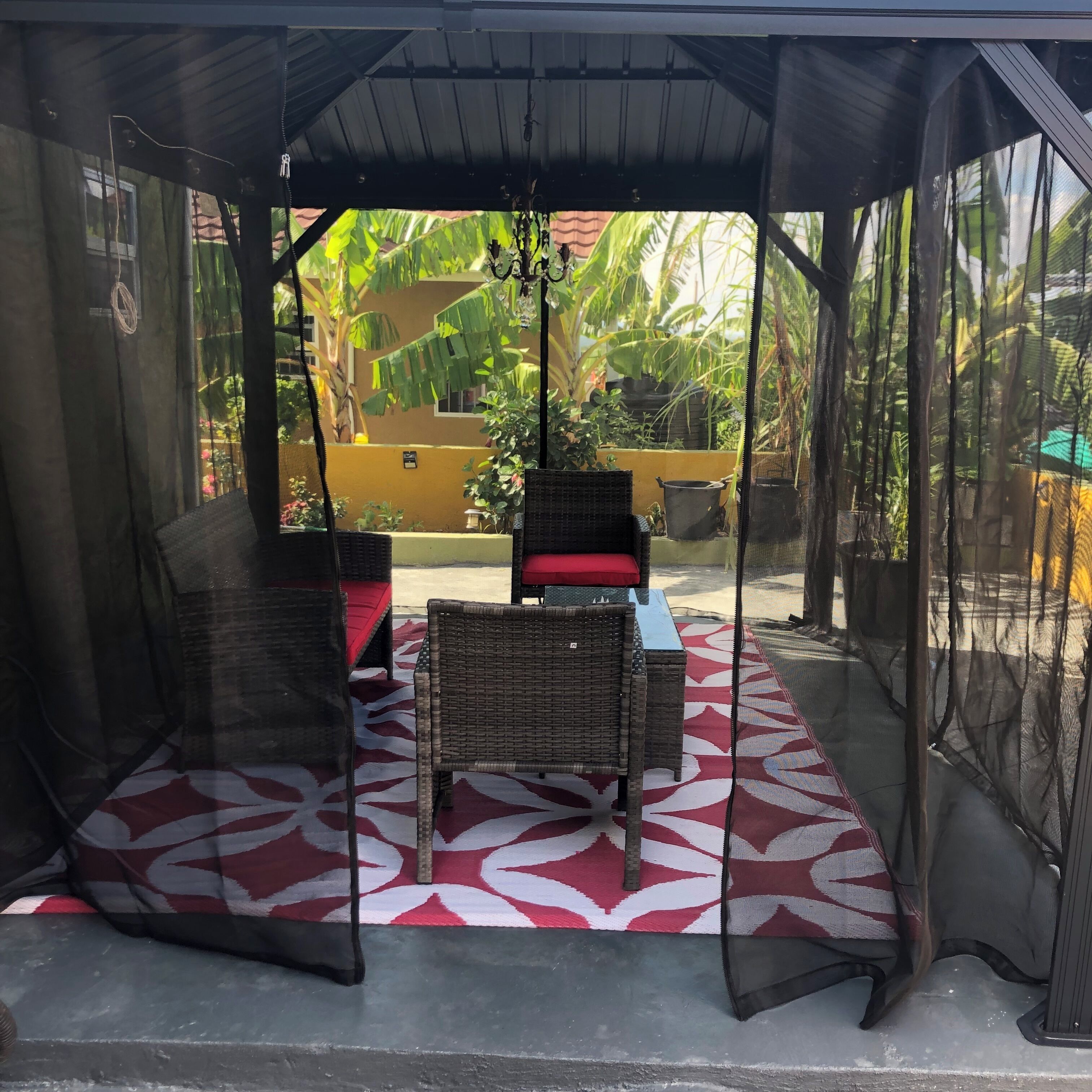 Un espacio de estar al aire libre con techo, mobiliario de mimbre y piso con estampado rojo y blanco.