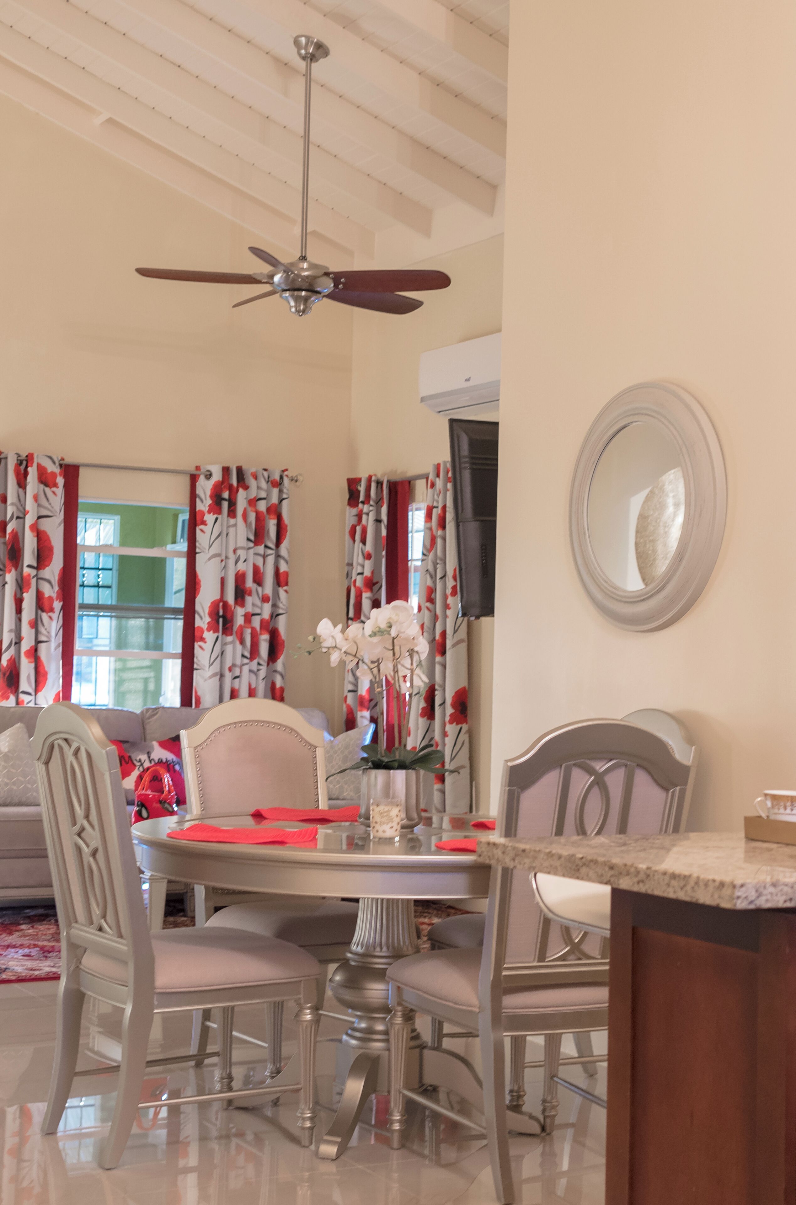 A dining area with a round table, chairs, a ceiling fan, and a mirror on the wall.