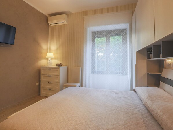 Une chambre d’hôtel avec un lit, une table de chevet avec une lampe, un téléviseur fixé au mur et une fenêtre donnant sur un paysage verdoyant.