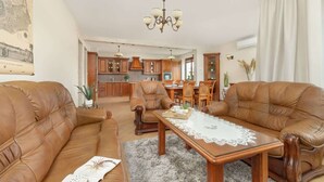 Ein geräumiges Wohnzimmer mit Ledersofas, einem Holztisch und einem Essbereich mit Holzsesseln und einem Kronleuchter.