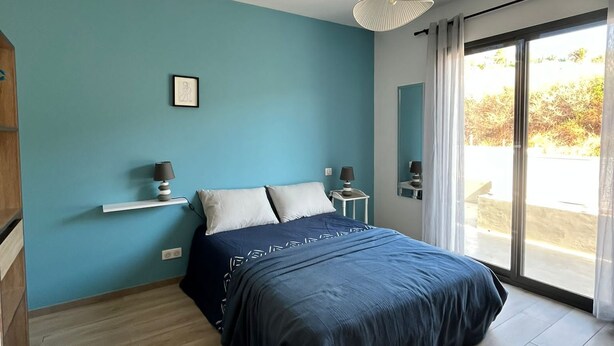 Un dormitorio con cama, mesita de noche, lámpara, marco de foto y ventana con cortinas.