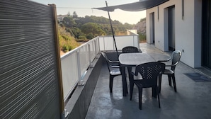 Un patio exterior moderno con mesa y sillas, un paraguas negro y vistas a una ladera.