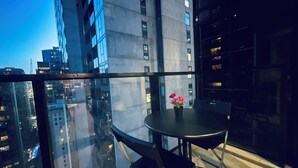 A modern dining area with a glass table and chairs, a vase with flowers, and a cityscape view through large windows.