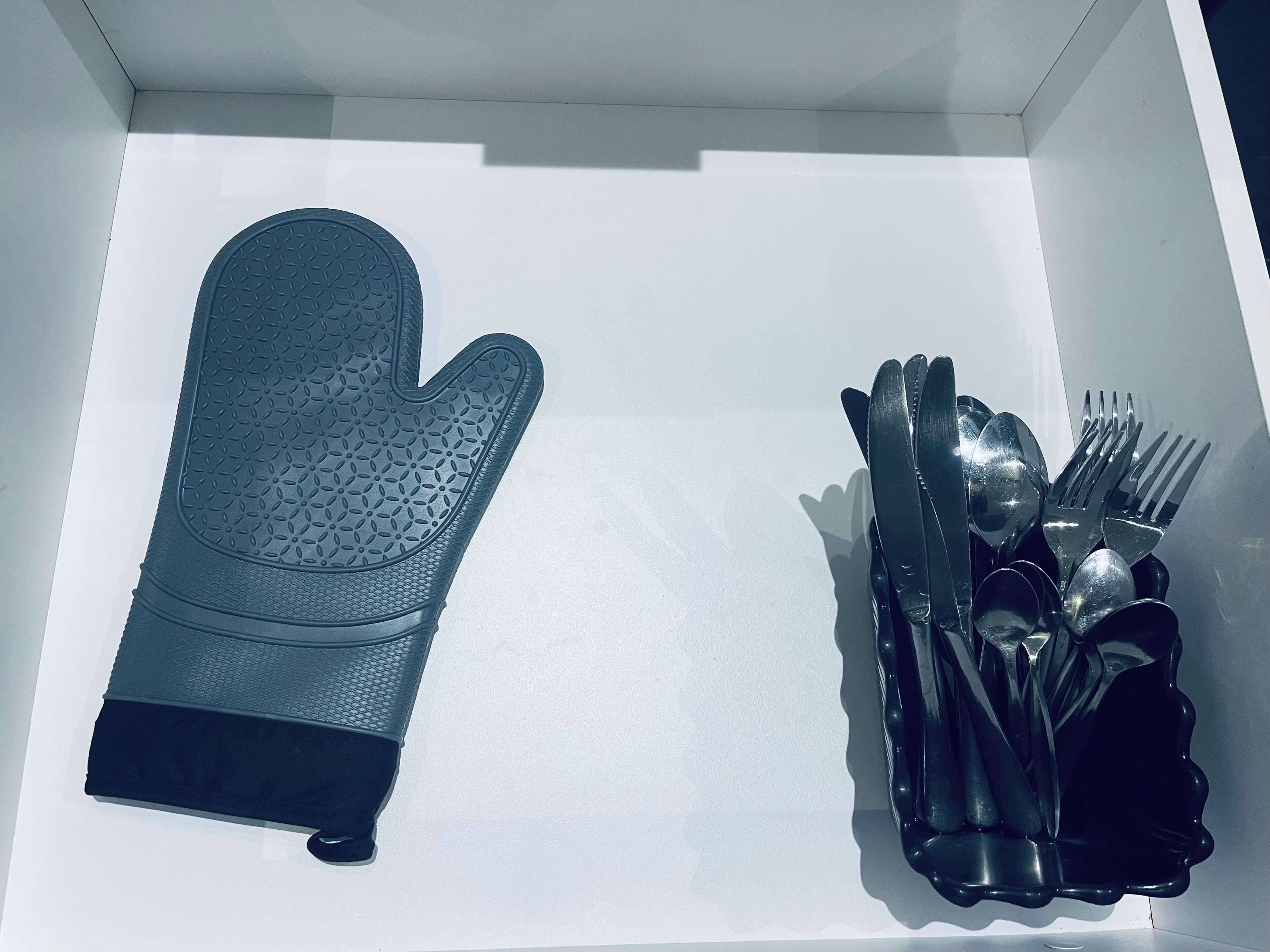 Eine Schublade mit einem schwarzen Topflappen und Besteck.