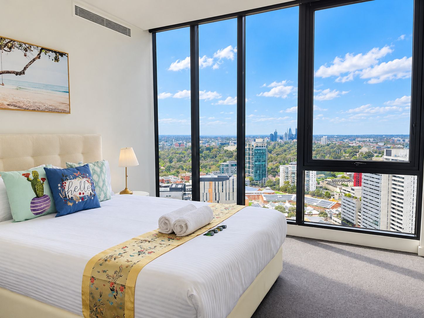 A hotel room with a large bed, a view of the city, and a painting on the wall.