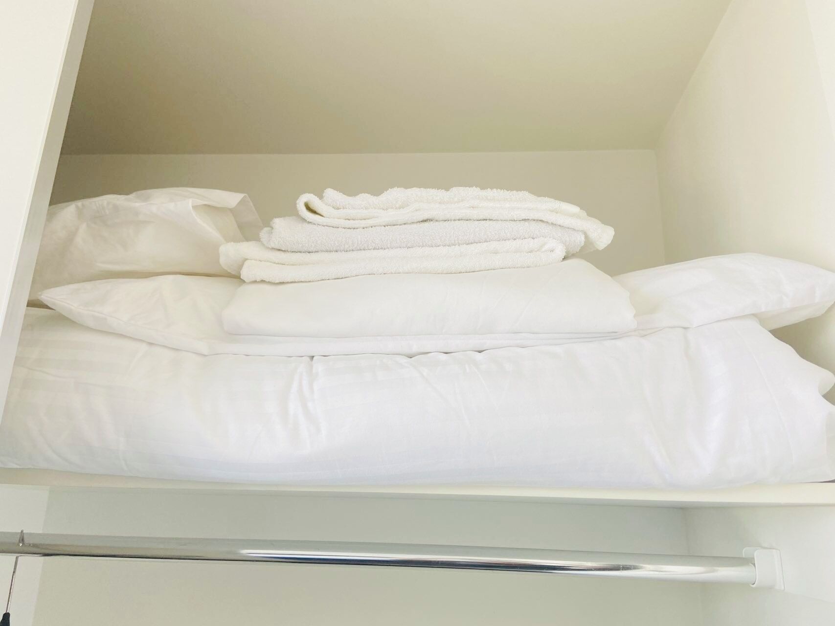 Un placard bien rangé, avec du linge de lit blanc et des serviettes pliées.