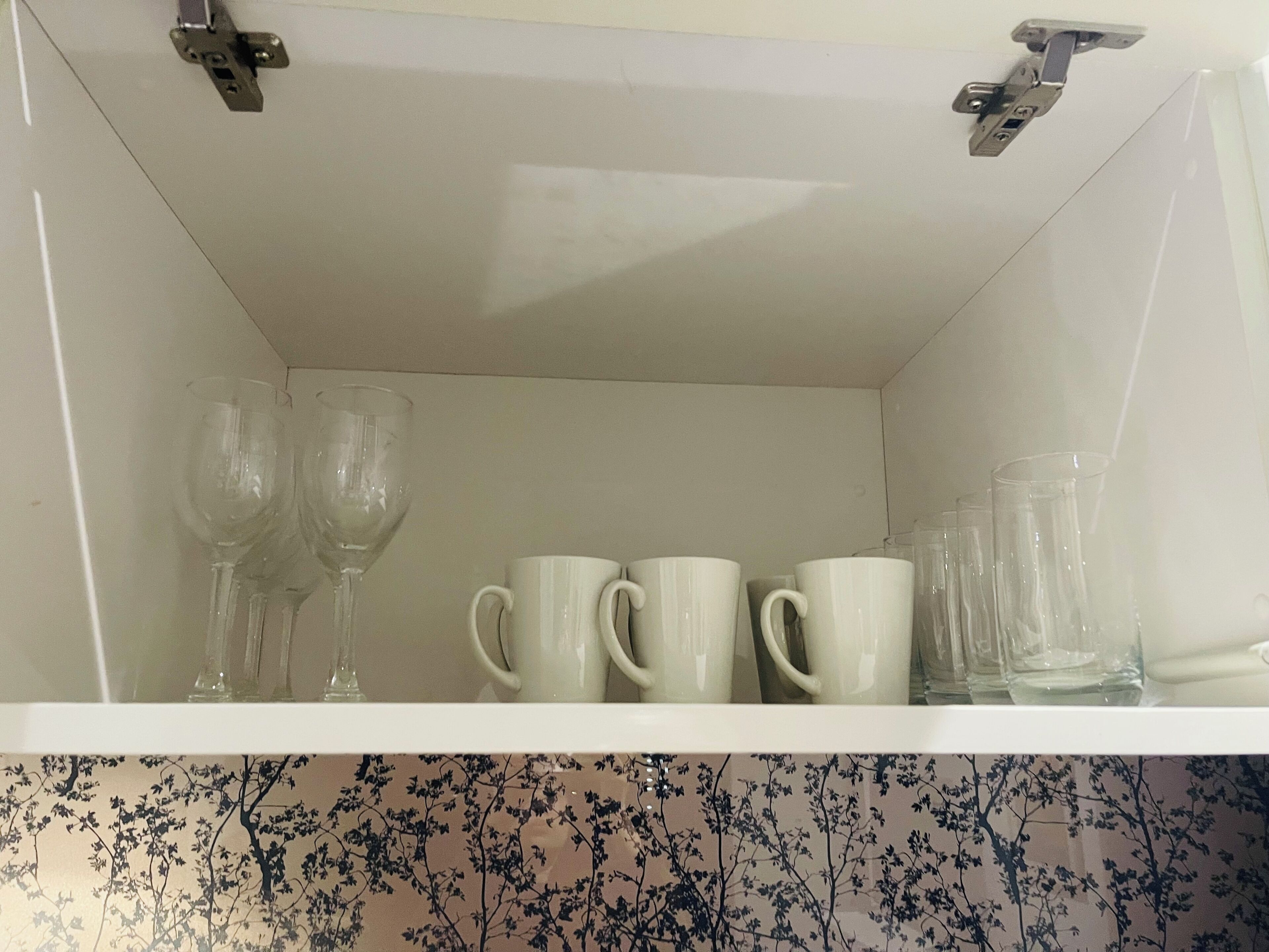 Une étagère blanche sur laquelle sont pos és trois verres à vin, deux tasses blanches et plusieurs verres transparents.
