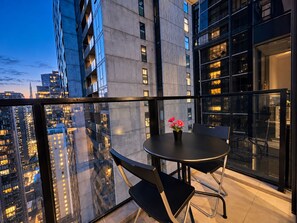 A balcony with a table and chairs, overlooking a cityscape at dusk.