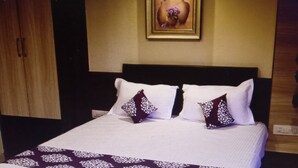A neatly made bed with white and patterned bedding, a dark headboard, and a framed picture above it. - HOTEL KAMBAA JAWAI (Sumerpur)