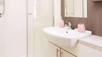 A bathroom with a white sink, a mirror, and a pink soap dispenser.