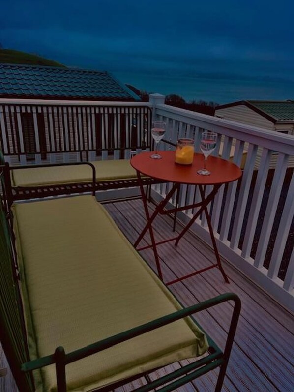 A deck with a round table and two cushioned chairs, a glass of red wine, and a bottle of orange juice. - Luxury Caravan sea Views Sleep 6 Free Wifi (Paignton)
