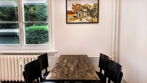 A dining area with a wooden table and black chairs, a radiator below the window, and a framed painting on the wall. - Schöne, Frisch Sanierte Ferienwohnung, Ideal für Familien Aufenthalte (Hamburg)