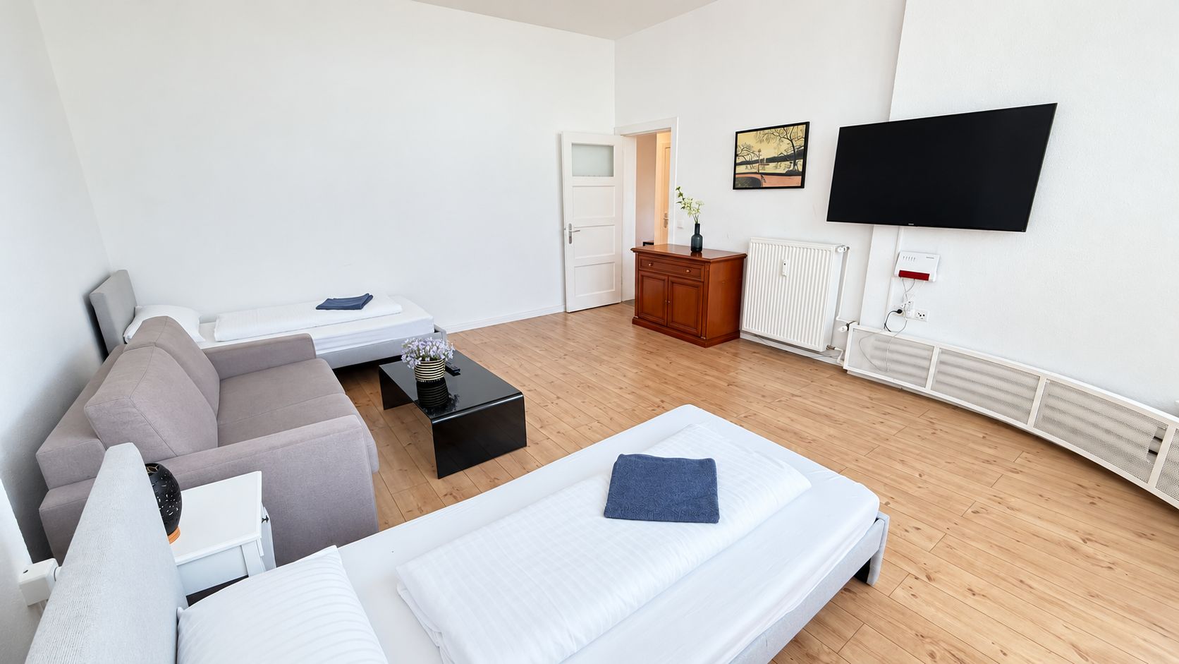 A hotel room with a sofa, two single beds, a coffee table, a TV, and a radiator.