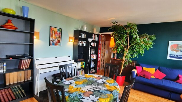 A living room with a piano, bookshelves, a blue sofa, and a dining table. - Quiet, bright apartment with private parking near central Paris (Paris)