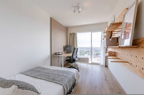 A modern hotel room with a bed, desk, and large window.