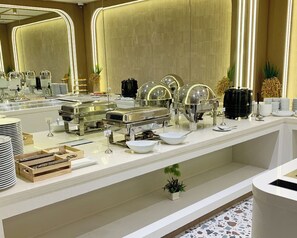Montaje de bufé con varias estaciones de servicio, que incluyen opciones de comida caliente y fría, y una variedad de platos exhibidos en una barra.